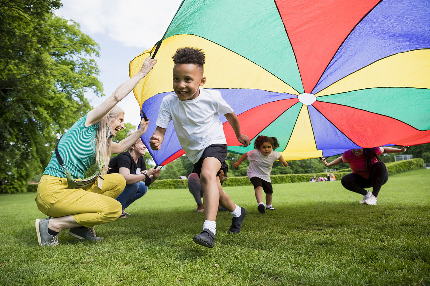 Children playing with a parachute at school during pe in the North East of England. A boy is running underneath it.