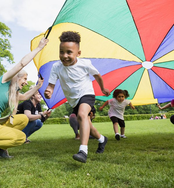 Children playing with a parachute at school during pe in the North East of England. A boy is running underneath it.